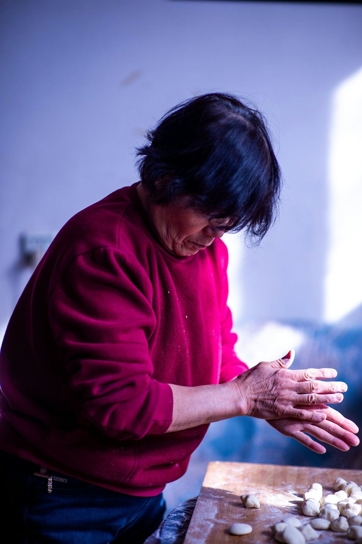 An older woman in a red jumper shaping dumpling dough by hand